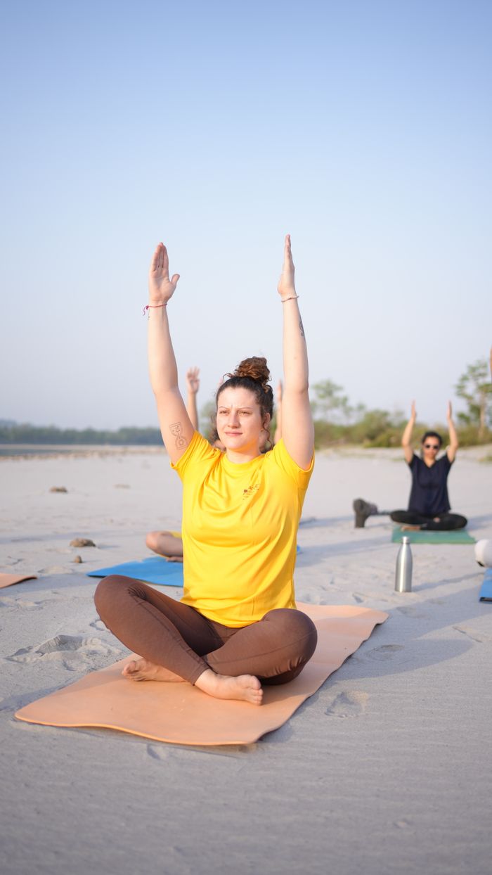 who-we-are Participants in a serene yoga class on a sandy beach, practicing morning asanas.