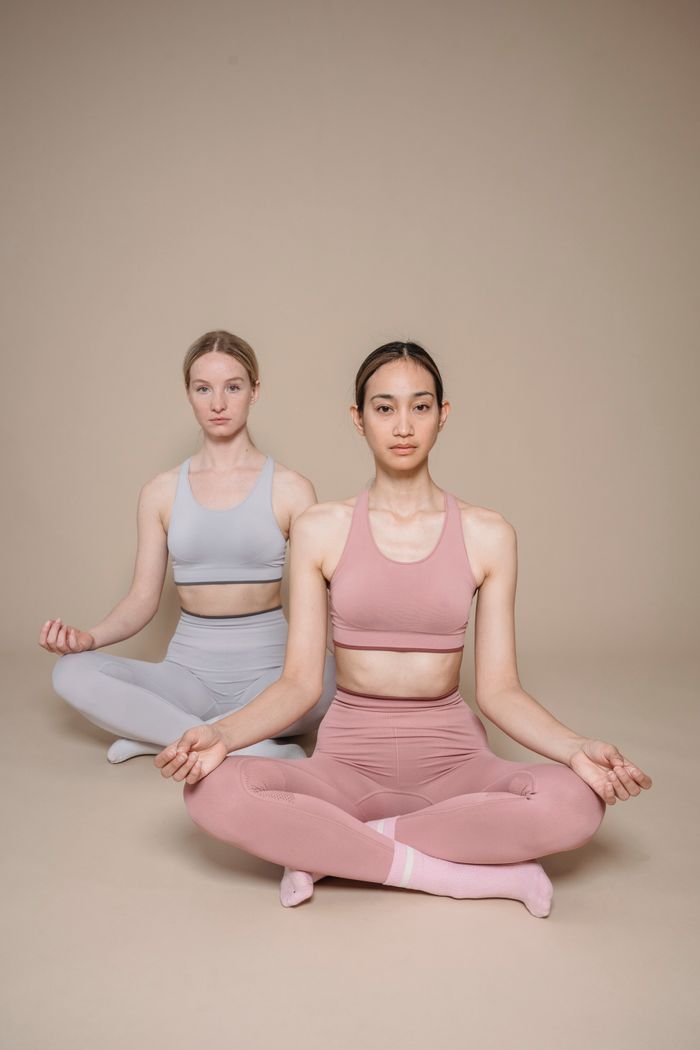team-02 Two women in activewear meditating indoors, focusing on mindfulness and wellness.